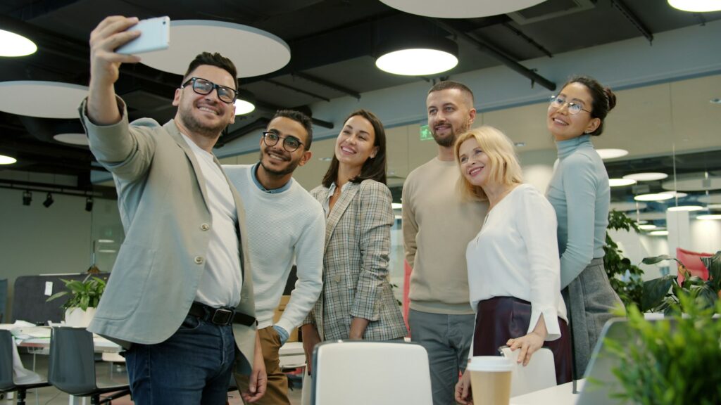 Kolleginnen und Kollegen machen im Büro gemeinsam ein Selfie mit dem Smartphone für den Employer-Branding-Kanal