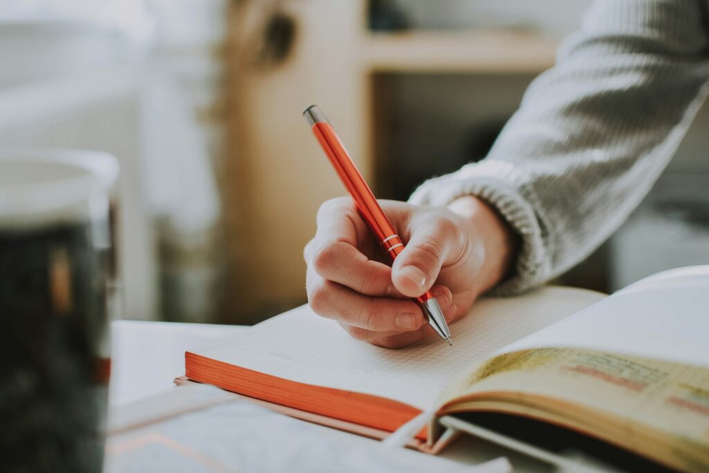 Hand schreibt mit rotem Stift Notizen in ein Buch als Vorbereitung auf die Gehaltsverhandlung im Marketing