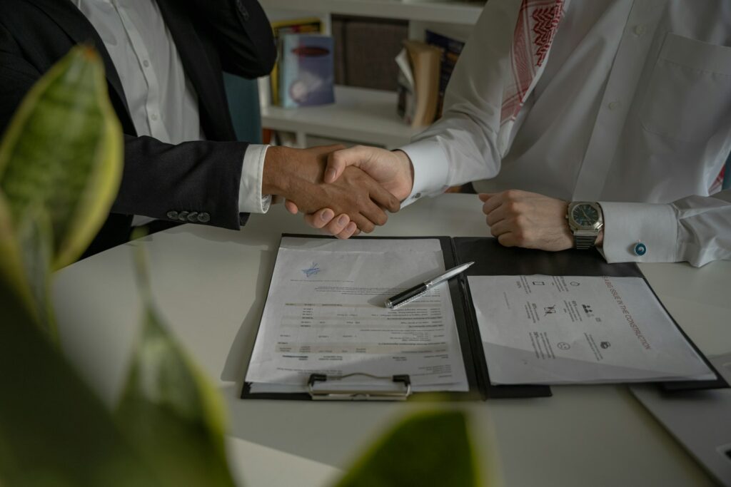 Zwei Personen reichen sich nach erfolgreicher Gehaltsverhandlung im Marketing über einem Dokument die Hand