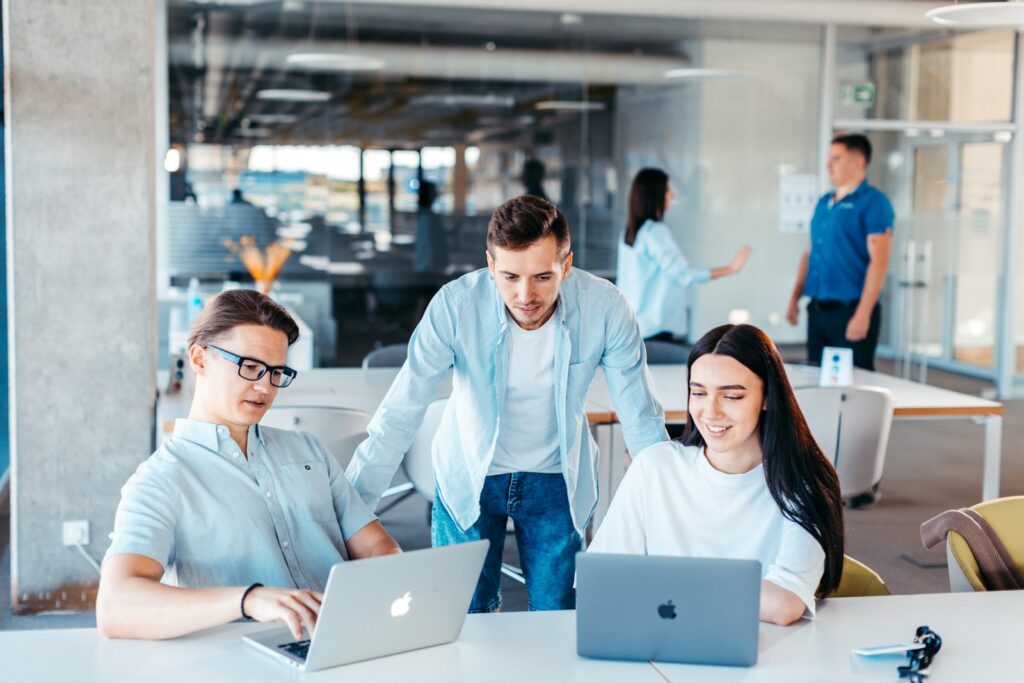 Junges Team an einem Tisch mit Laptops bespricht neue Einträge für die Prompt-Bibliothek