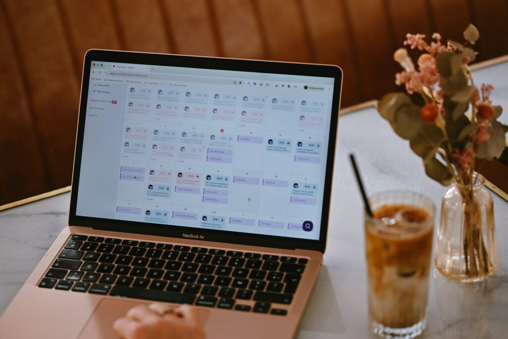 Laptop mit geöffnetem Social-Media-Content-Kalender neben einem Glas Eiskaffee – digital einen Redaktionsplan erstellen