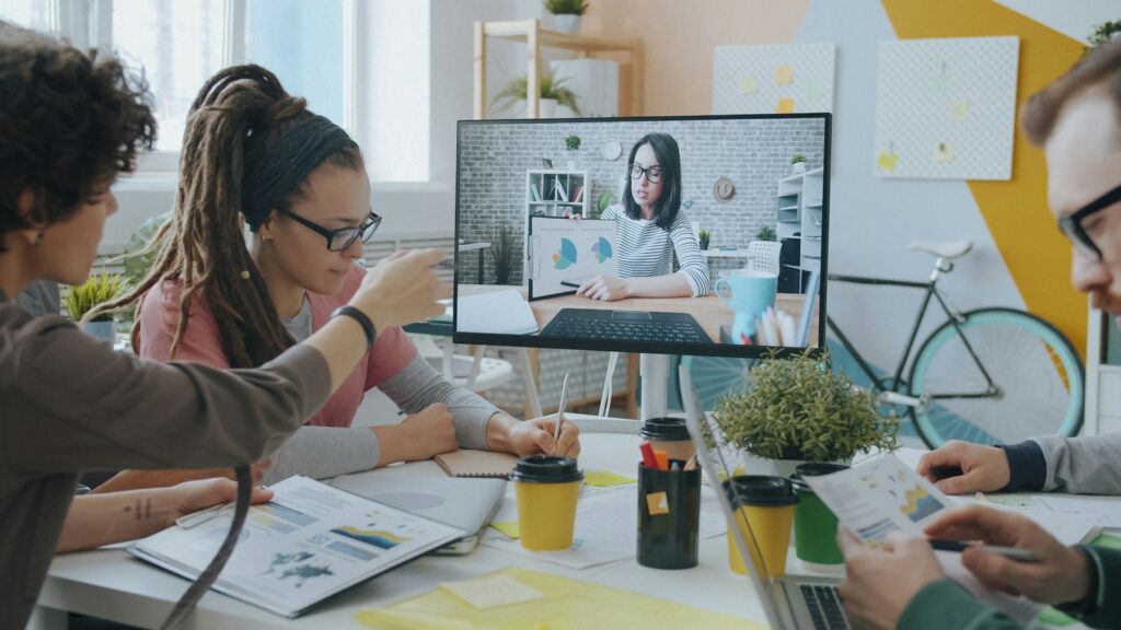 Gruppe im Meetingraum spricht per Videocall mit einer Kollegin im Rahmen von Remote Leadership