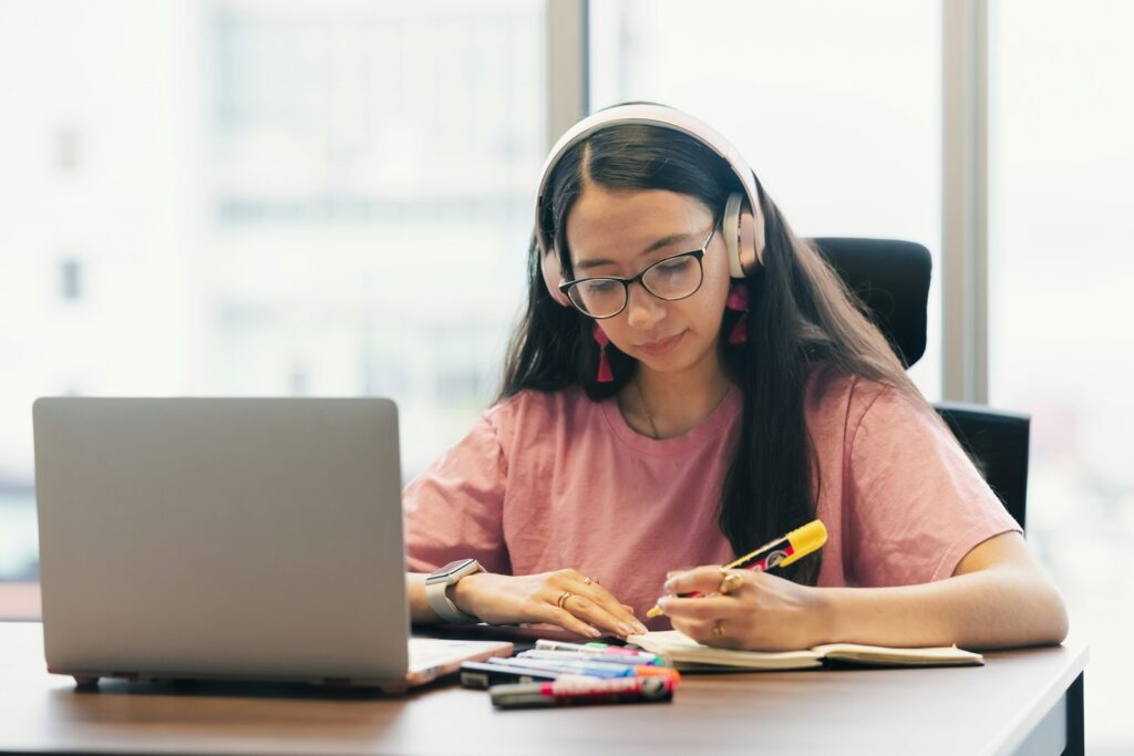 Junge Frau mit Kopfhörern lernt am Schreibtisch für ihre Weiterbildung im Marketing